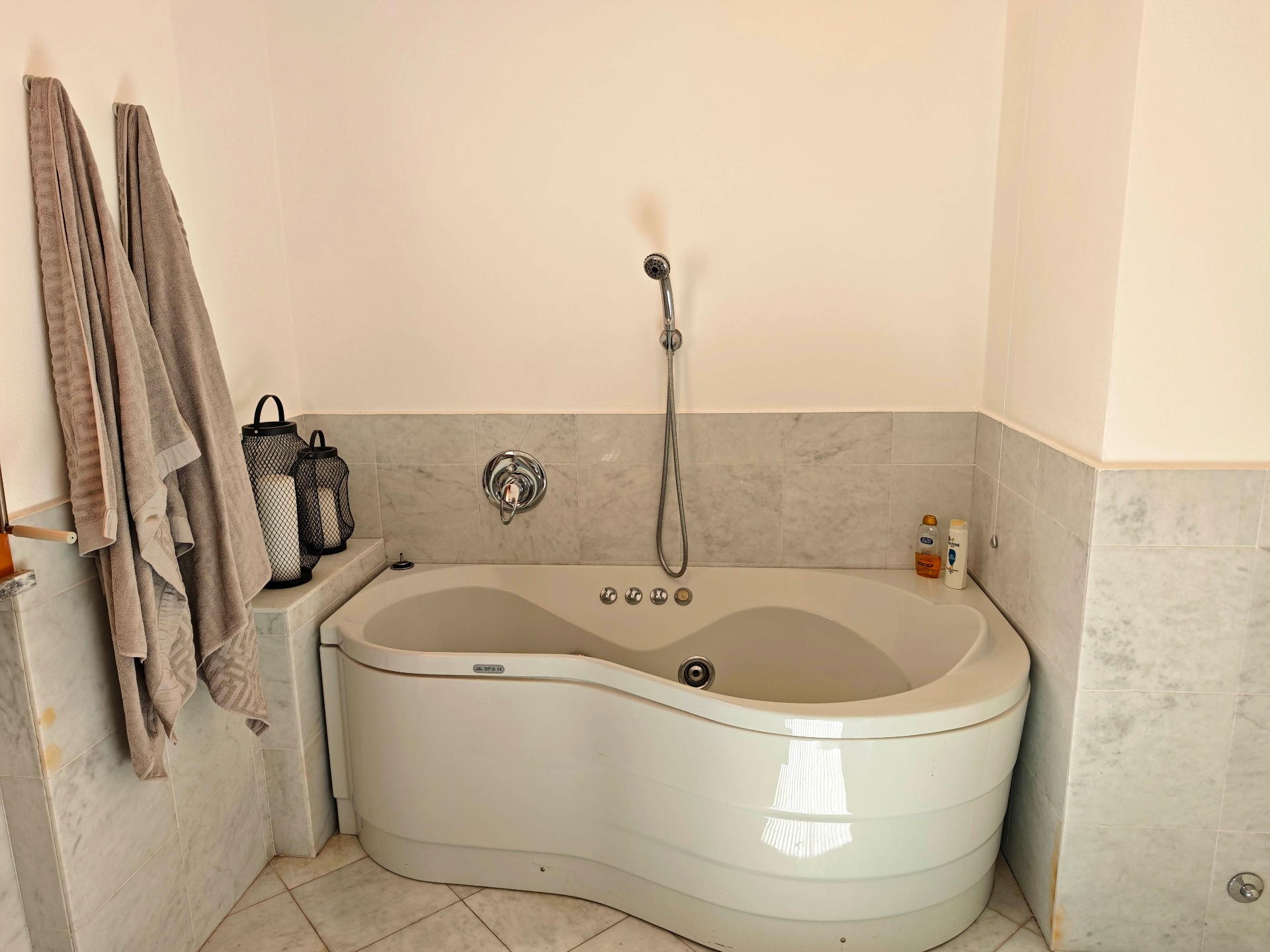 Curved whirlpool bath with hand shower, marble tiling and soft towels