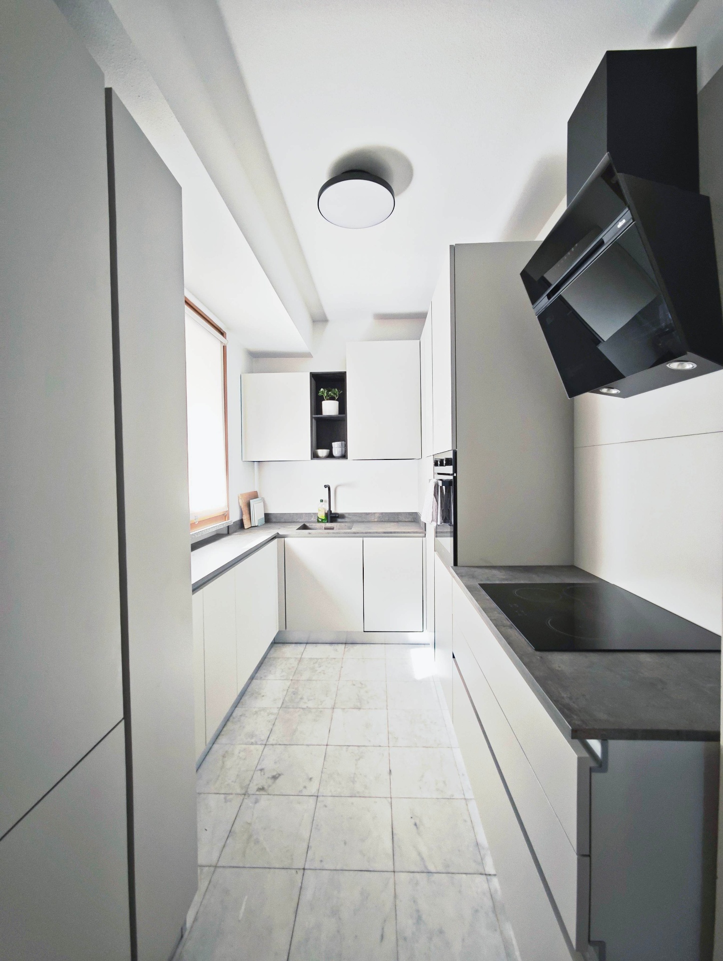Modern white galley kitchen with marble floor, induction hob and black hood