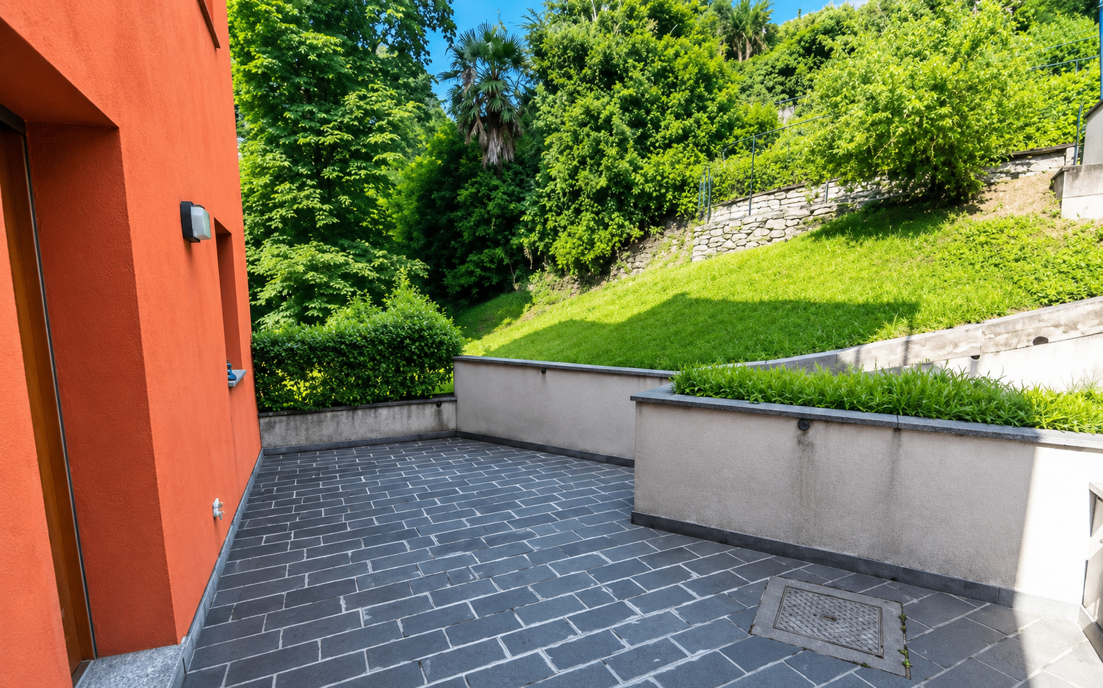 Stone-paved garden terrace beside the orange villa wall with sloped lawn behind