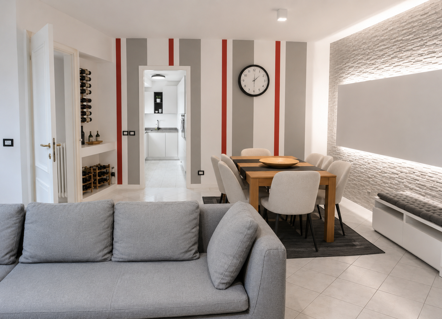 Open-plan living and dining room with grey sofa, wooden dining table and a striped feature wall leading to the kitchen